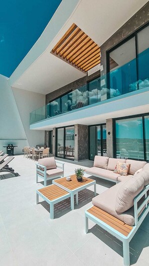 Una casa moderna con balcón, mobiliario exterior y ventanas amplias.