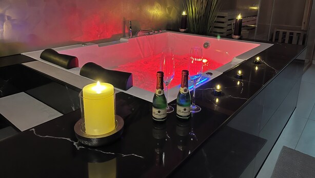 Ein moderner Wellnessbereich mit Pool, Kerzen und Weinflaschen auf einer Marmorplatte.