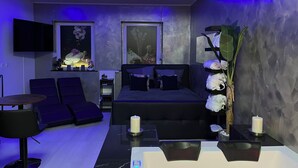 Ein modernes Schlafzimmer mit einem Bett, einem Sofa, einem Fernseher und einem Schreibtisch mit einem Computer.