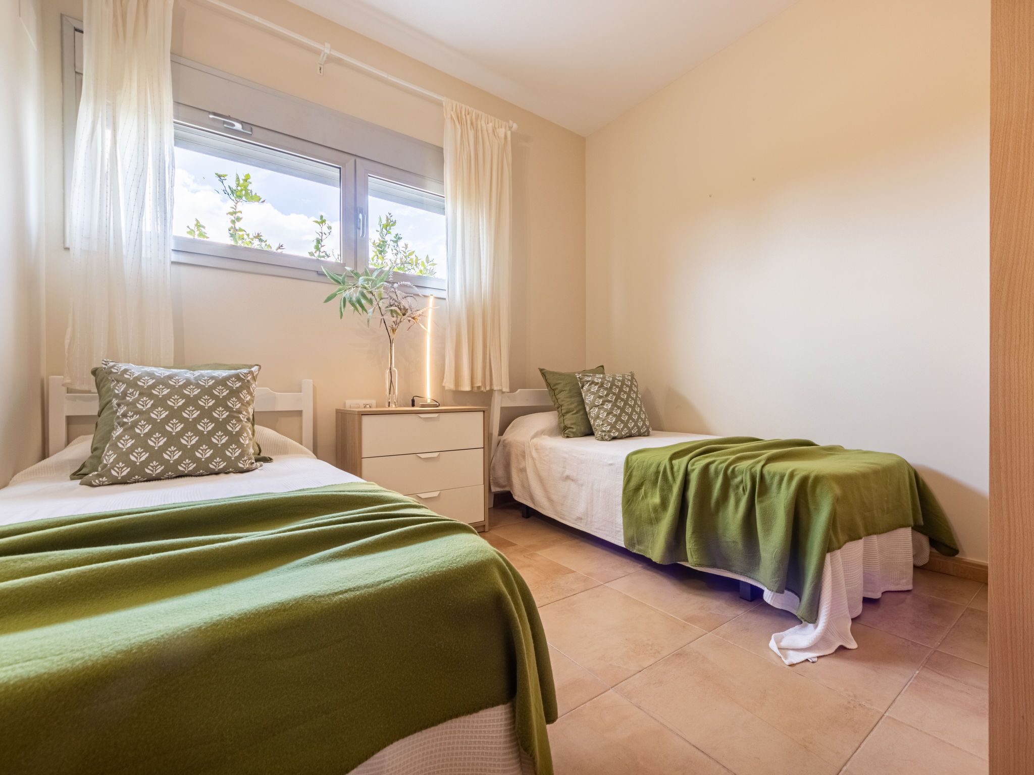 A bedroom with two beds, a nightstand, a bedside table, and a window with curtains.