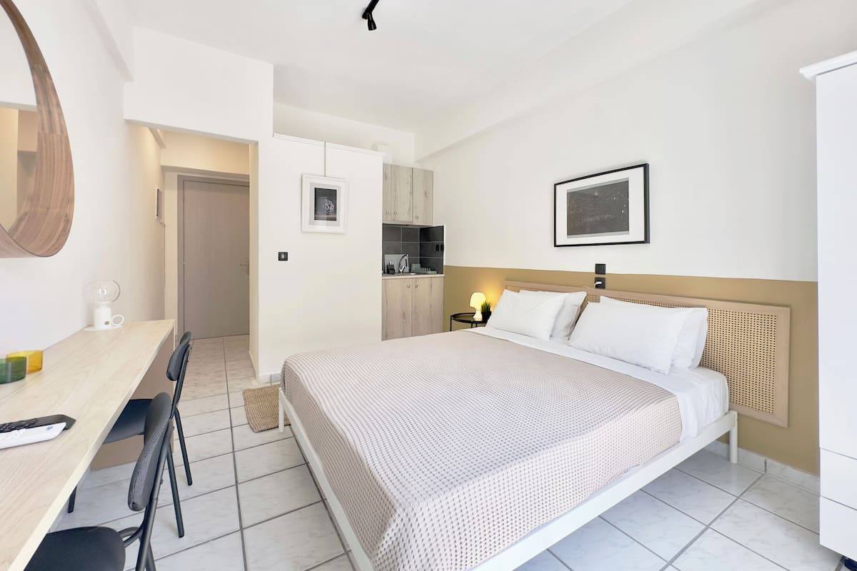 A modern hotel room with a bed, a desk, and a kitchenette.