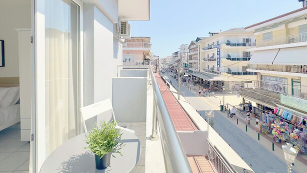 A balcony with a potted plant, overlooking a street with shops and a hotel. - Seagull by halu! (Katerini)