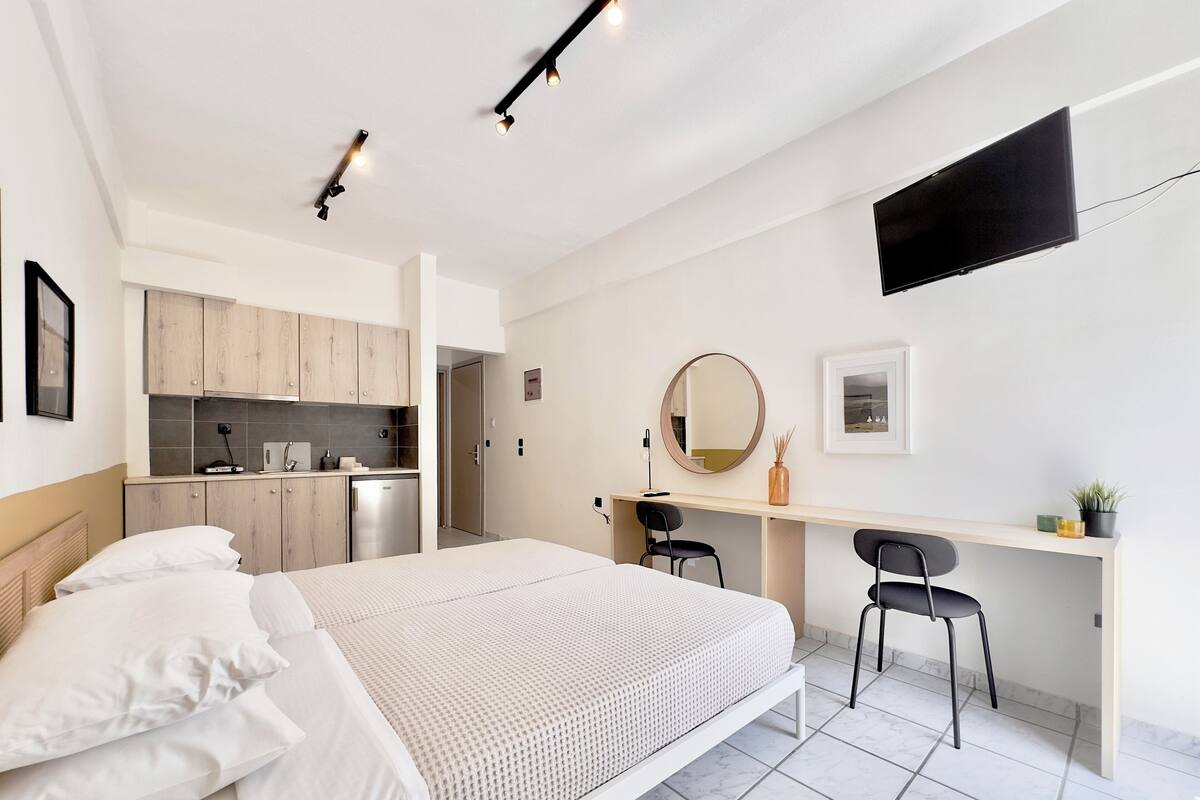 A modern bedroom with a bed, a desk, and a kitchenette.