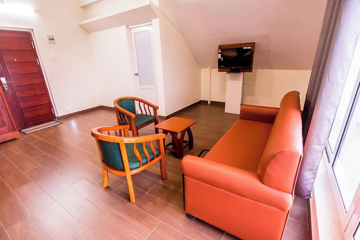 A living room with a wooden sofa, two wooden chairs, a small table, and a television on the wall.