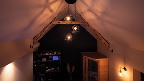 A room with a sloped ceiling, wooden beams, and geometric pendant lights. - Chambre d'hôte with private spa, whirlpool bath and infrared sauna (Boëseghem)
