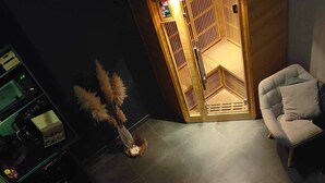 A modern bathroom with a large bathtub, a seating area with a chair, and a wooden partition with a control panel. - Chambre d'hôte with private spa, whirlpool bath and infrared sauna (Boëseghem)