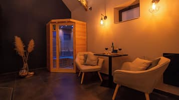 Une chambre moderne équipée d’un sauna, de deux fauteuils, d’une petite table avec une bouteille et décorée de quelques touffes d’herbe des pampas.