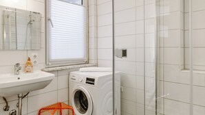 Een moderne badkamer met een douchecabine van glas, een ingebouwd wastafelmeubel, een wasmachine en een klein mandje in oranje.