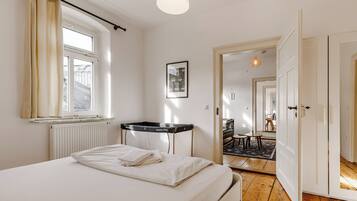 Une chambre à coucher avec un lit, une fenêtre avec des rideaux, un radiateur, un bureau et une porte donnant sur une autre pièce.