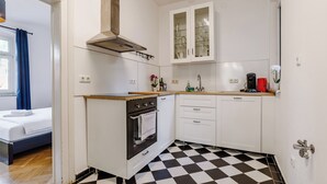 Een compacte keuken met een zwart-wit geruite vloer, een ingebouwde oven, witte kastjes en een klein aanrecht.
