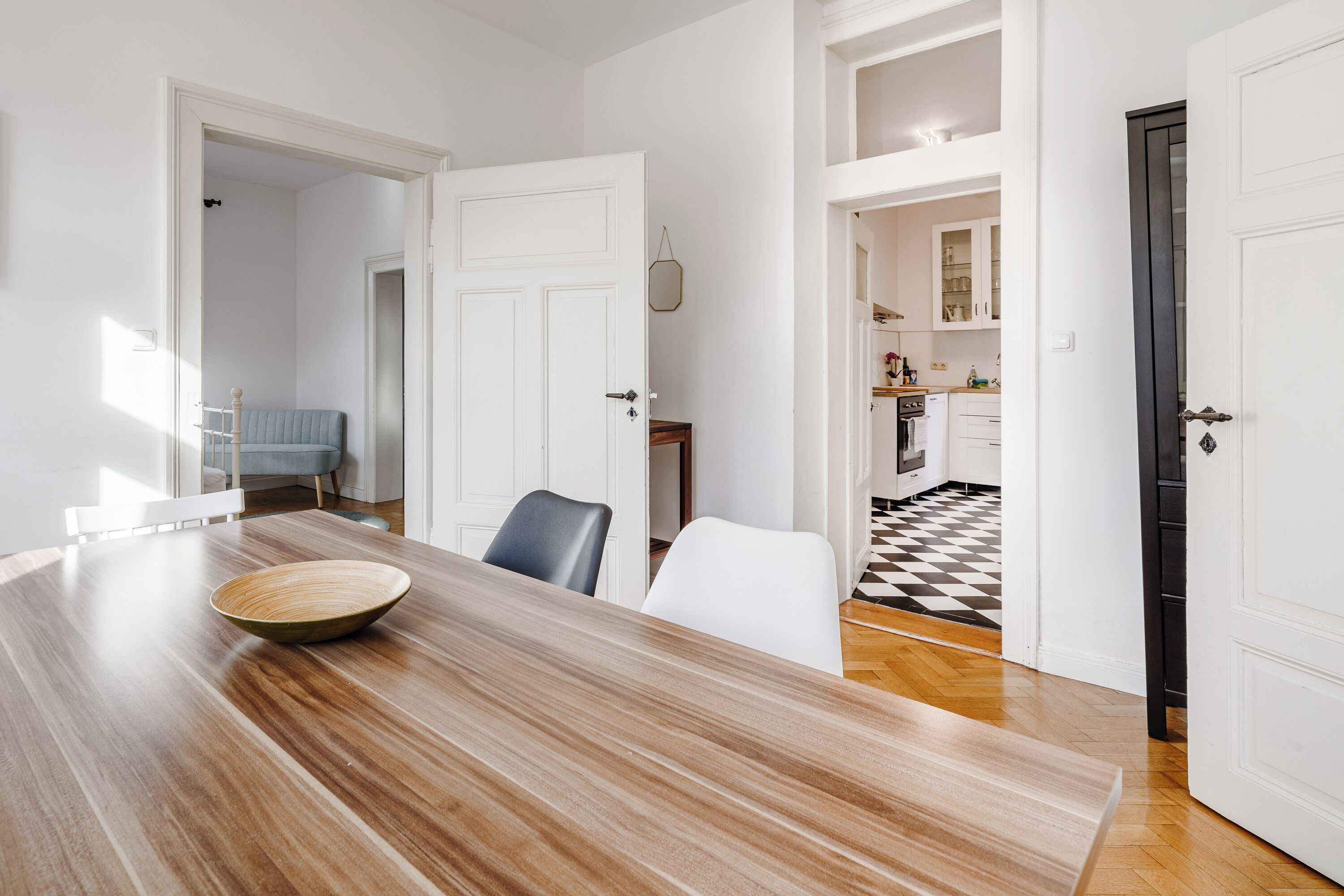Un coin repas avec une table et des chaises en bois, un bol posé sur la table et des murs blancs.