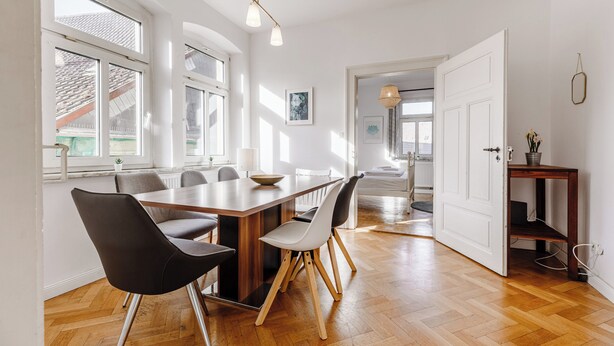 Een eethoek met een houten tafel en stoelen, grote ramen en uitzicht op buiten.