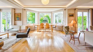 A spacious room with a large dining table, multiple chairs, and a view of greenery through large windows. - Villa de charme à Benerville - 5 Suites, Garden 1800m² & Beach on foot (Benerville-sur-Mer)
