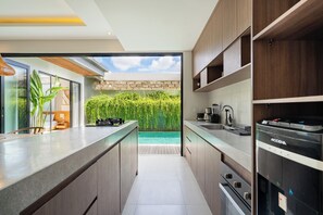 A modern kitchen with a built-in island, a view of a swimming pool, and a brick wall. - Yoki Villa by Betterplace (Canggu)