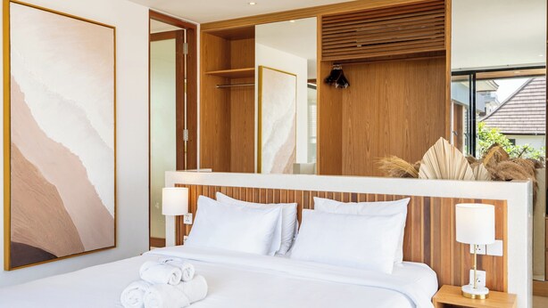 A modern hotel room with a large bed, a wooden headboard, a large mirror, and a view of the outside. - Yoki Villa by Betterplace (Canggu)