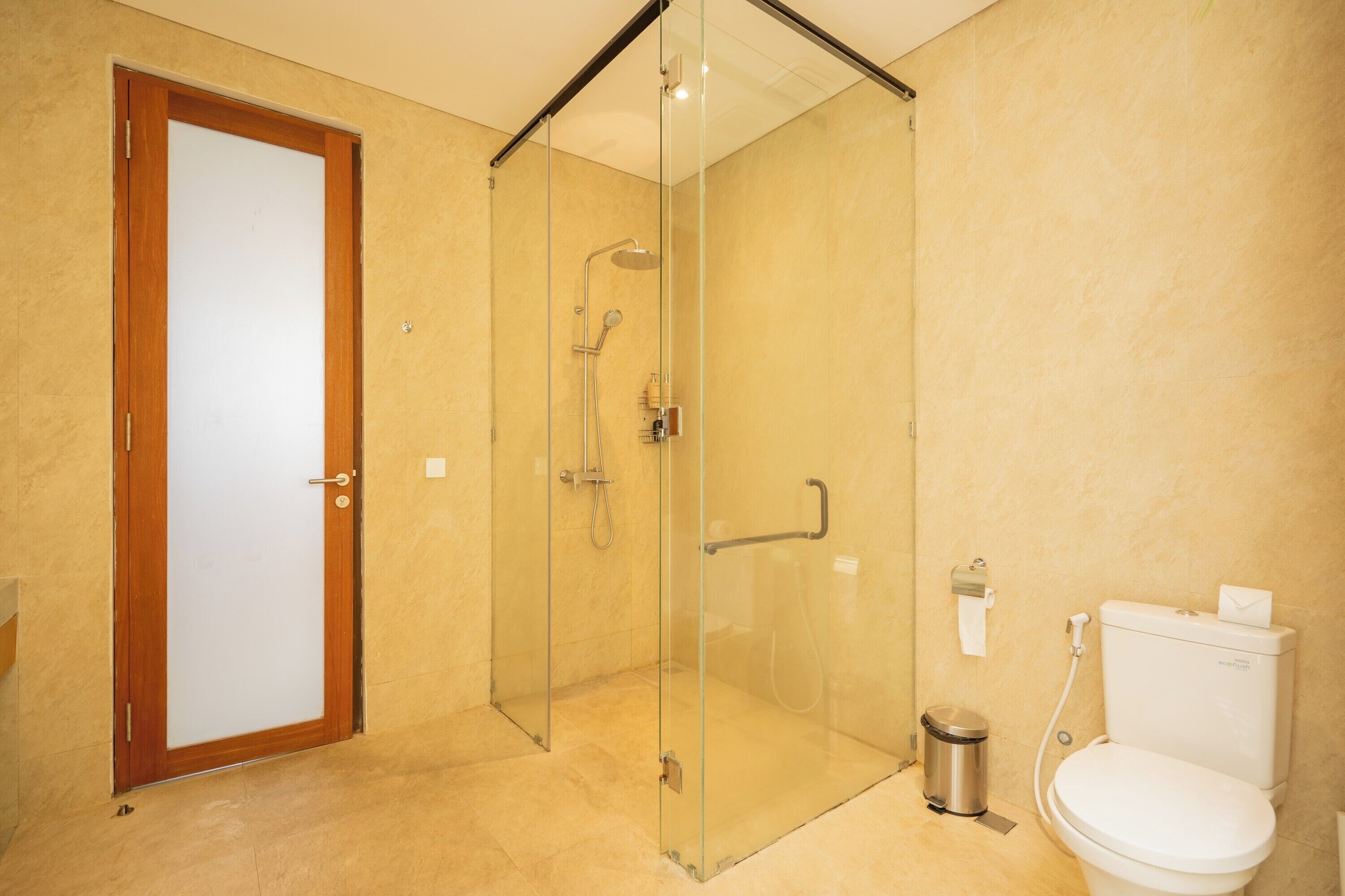 A modern bathroom with a glass-enclosed shower, a white toilet, and a trash bin.