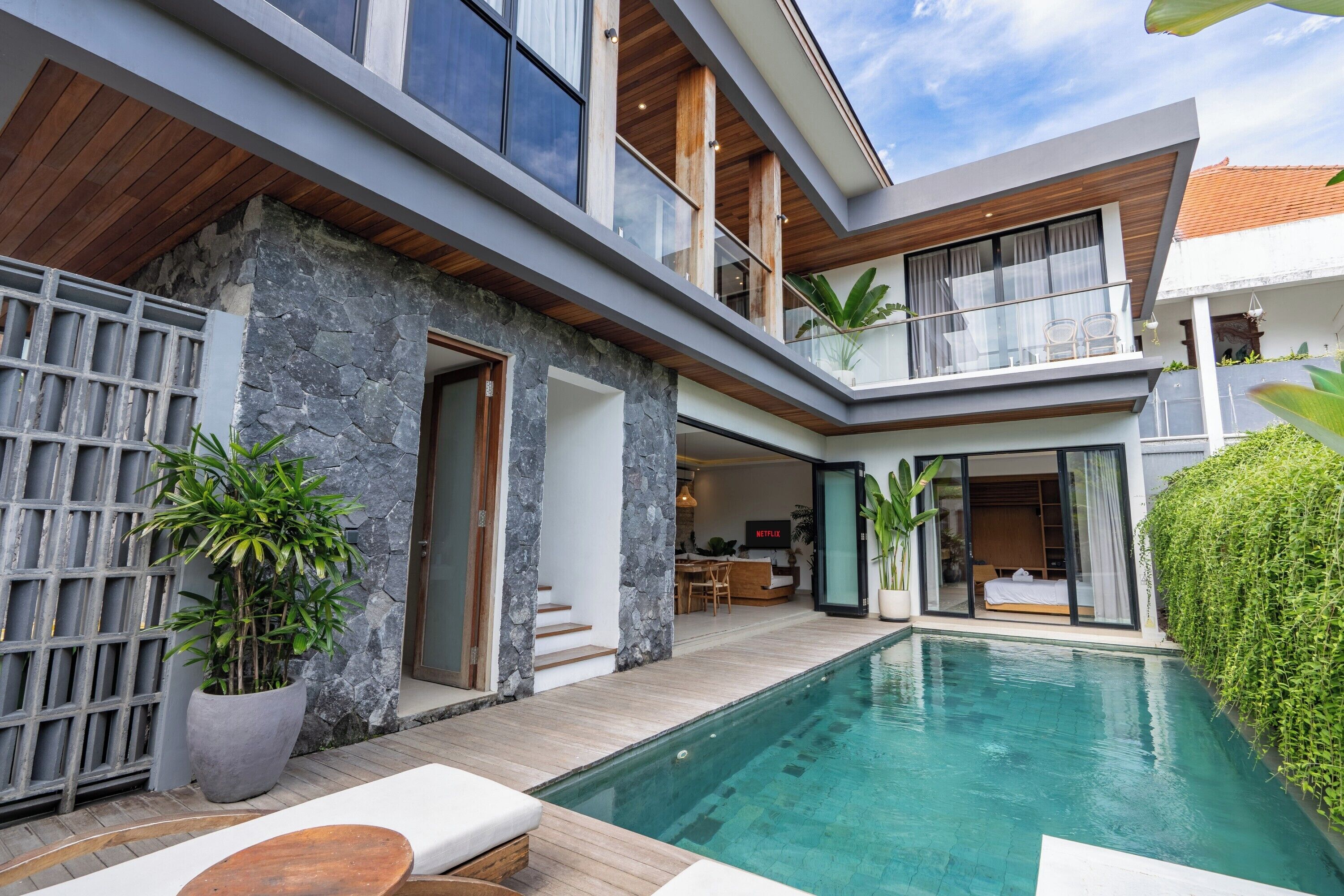 A modern multi-level house with a swimming pool, stone walls, and a balcony.