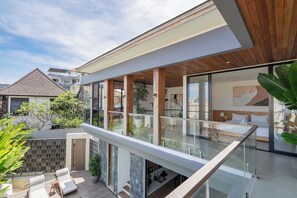A modern hotel with a spacious balcony, a kitchen area, and a bedroom with a large window. - Yoki Villa by Betterplace (Canggu)