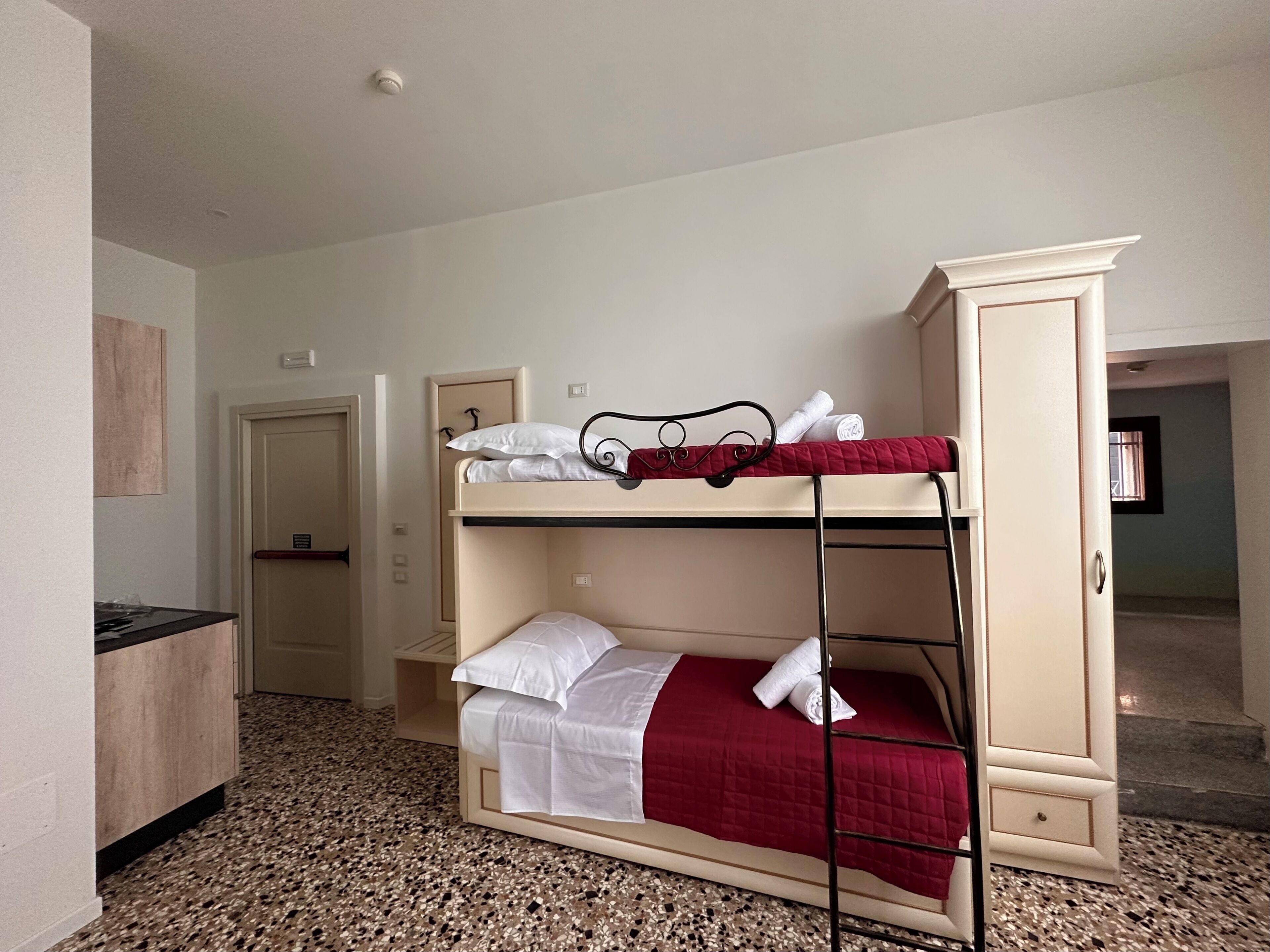 Une chambre avec un lit superposé, une armoire, une porte et une petite table.