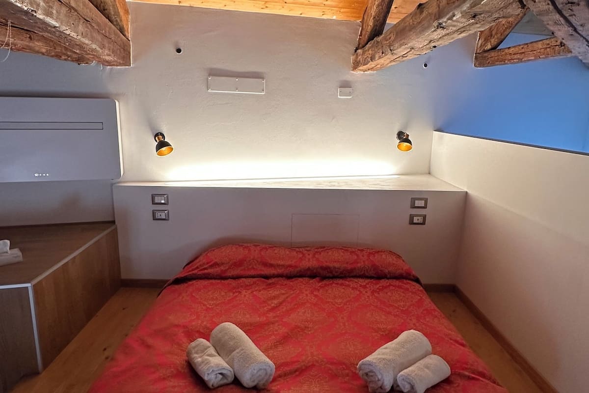A small, cozy room with a bed, two bedside lamps, and a wooden ceiling.