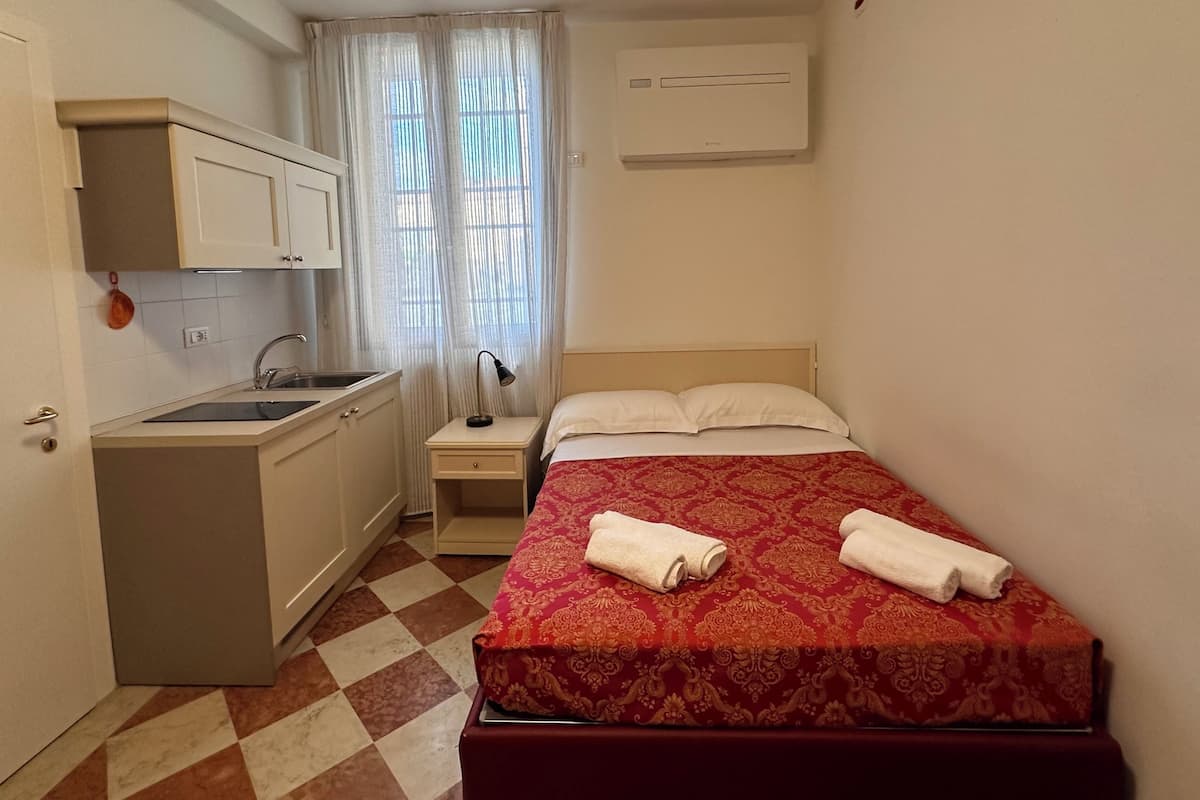 A compact hotel room with a bed, a small desk, a sink, and a window with curtains.