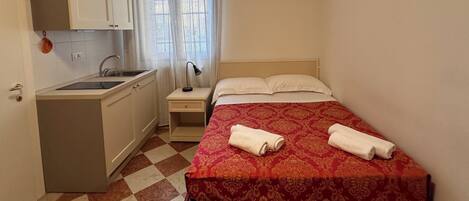Habitación de hotel pequeña con cama, un escritorio, un lavamanos y una ventana con cortinas.