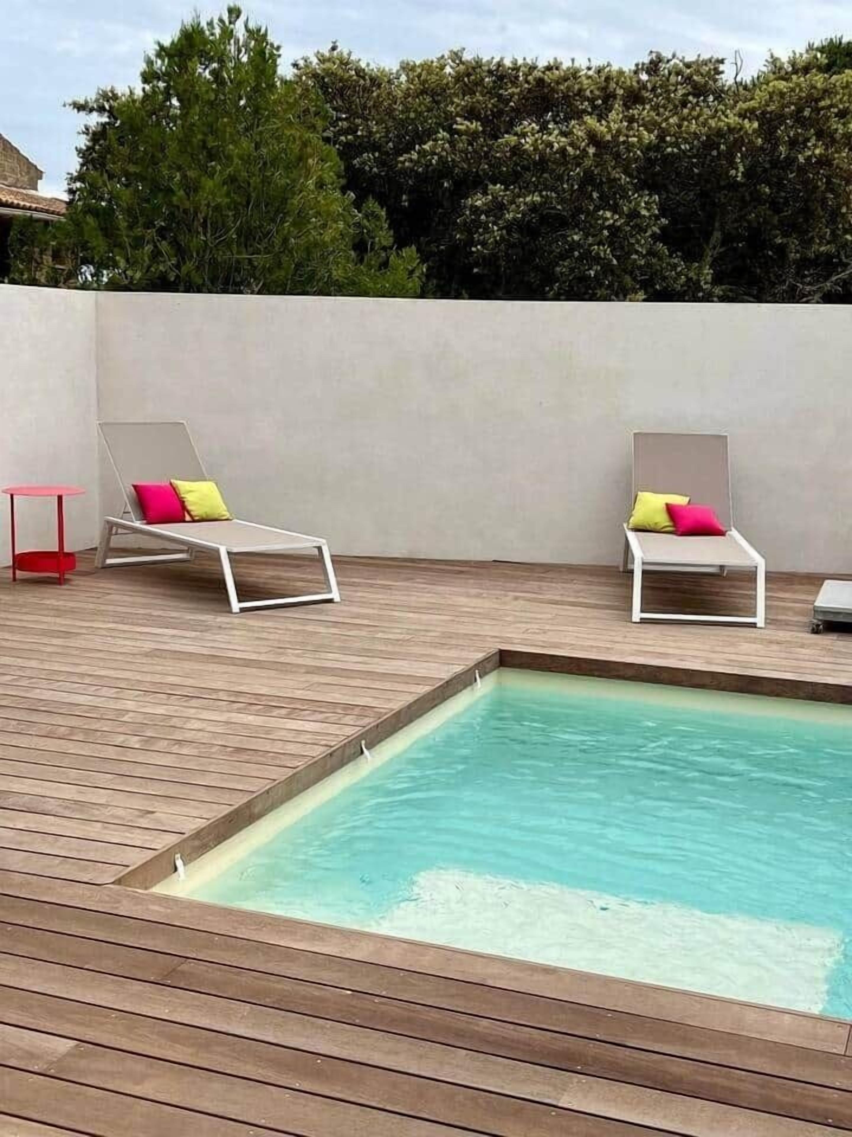 Ein Swimmingpool mit zwei Liegestühlen, jeweils mit einer Polsterauflage.