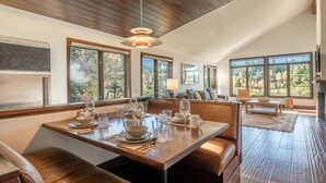 A dining area with a wooden table set for four, large windows, and a fireplace. - Snowcreek Townhome with Back Deck, Foosball Table, and Mountain Views! (Mammoth Lakes)