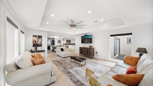 A spacious living room with a ceiling fan, a sofa set, a coffee table, and a television.