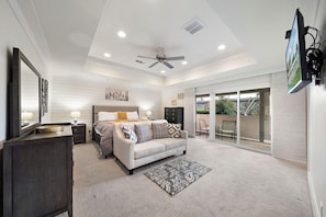 A bedroom with a bed, a nightstand, a dresser, a ceiling fan, and a large window.