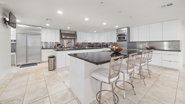 A modern kitchen with white cabinets, stainless steel appliances, and a central island with bar stools.