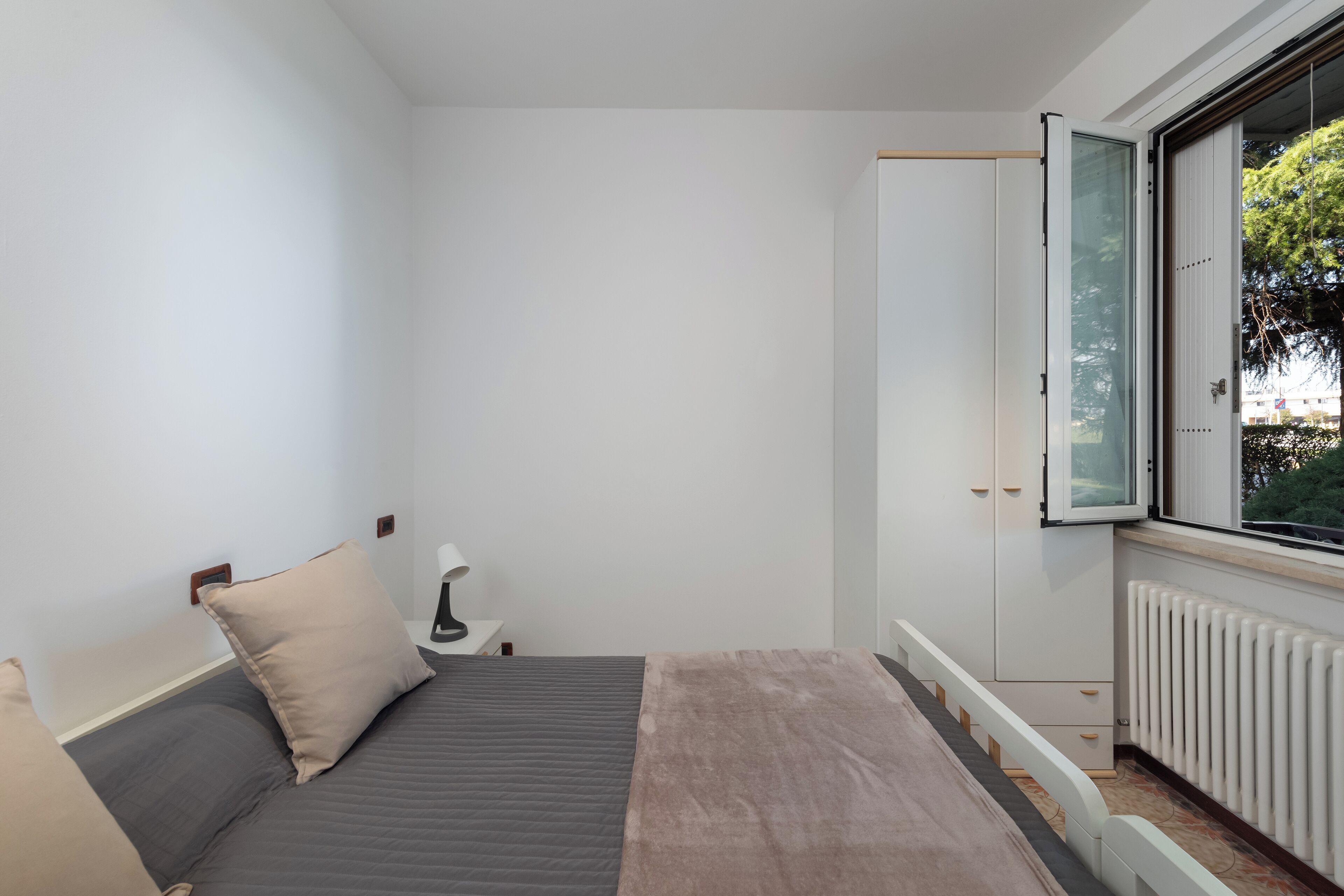 A bedroom with a bed, a nightstand, a window with a view, and a radiator.