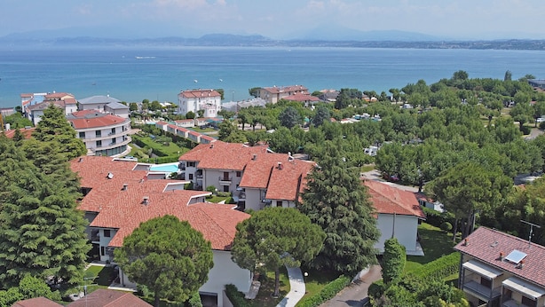 A coastal residential area with red-tiled roofs, green trees, and a view of the sea. - Residence Sant Elena A19 by Wonderful Italy (Peschiera del Garda)