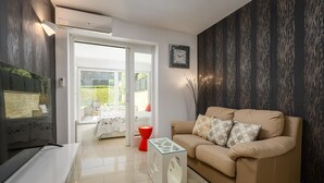 Ein modernes Wohnzimmer mit einem beigefarbenen Sofa, einem Glastisch, einem roten Hocker und einer Wanduhr.