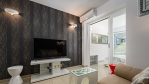 Ein modernes Wohnzimmer mit Flachbildfernseher, Glastisch, Sofa und weißem Beistelltisch.