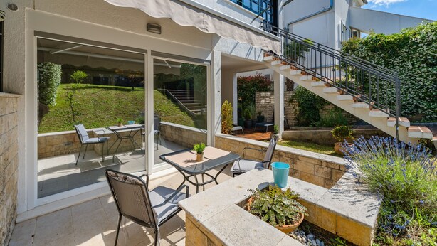 Eine überdachte Terrasse mit Gartenmöbeln, eine Treppe zu einer oberen Ebene und ein Gartenbereich mit Pflanzen.