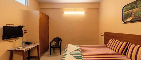 A hotel room with a bed, a TV, a desk with a chair, and a painting on the wall.