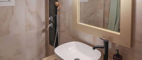 A modern bathroom with a white sink, a handheld showerhead, and a mirror with lights.