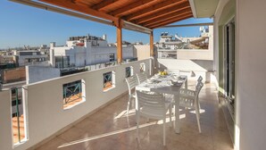A balcony with a table and chairs, a view of the cityscape, and a wooden ceiling. - Luminous Penthouse big veranda by GHH (Athens)