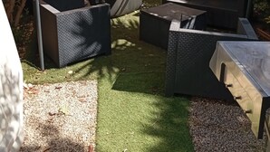 Un espace patio aménagé avec du mobilier d’extérieur, un coin salon couvert et une vue sur un bâtiment en arrière-plan.