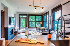 A modern kitchen with a large island, wine glasses, and a bottle of wine. - Lakefront, Mountain View - 1 Bedroom Resort Suite (Lac-Supérieur)