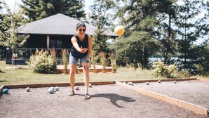 A person playing croquet in an outdoor setting with a house in the background. - Lakefront & Mountain View - 1 Bedroom Resort Suite (Lac-Supérieur)