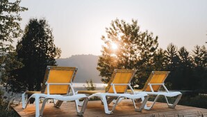 Two white lounge chairs with yellow cushions on a wooden deck overlooking a body of water with trees in the background. - Lakefront & Mountain View - 1 Bedroom Resort Suite (Lac-Supérieur)