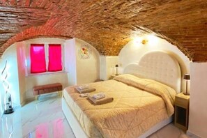 Un dormitorio con techo abovedado, una cama con cabecera blanca, un banco y una pared con un ventanal rojo.