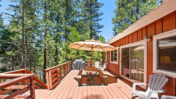 A wooden deck with a table and chairs, surrounded by a railing, and overlooking a forested area. - Rustic retreat in a convenient location! (Shaver Lake)