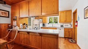 A kitchen with wooden cabinets, a white countertop, a kettle, a microwave, and a dishwasher. - Rustic retreat in a convenient location! (Shaver Lake)