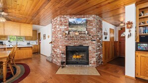 A cozy kitchen with a brick fireplace, wooden cabinets, and a dining area with a rug. - Rustic retreat in a convenient location! (Shaver Lake)