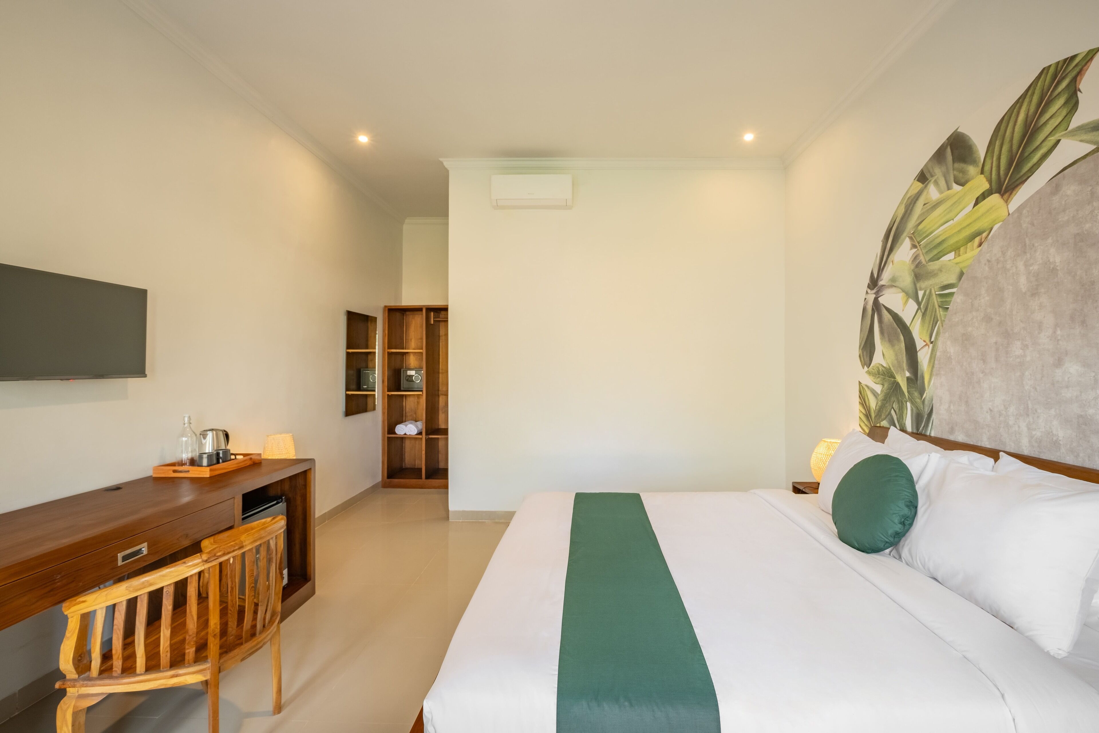 A hotel room with a bed, a desk, a chair, a wardrobe, and a large plant.