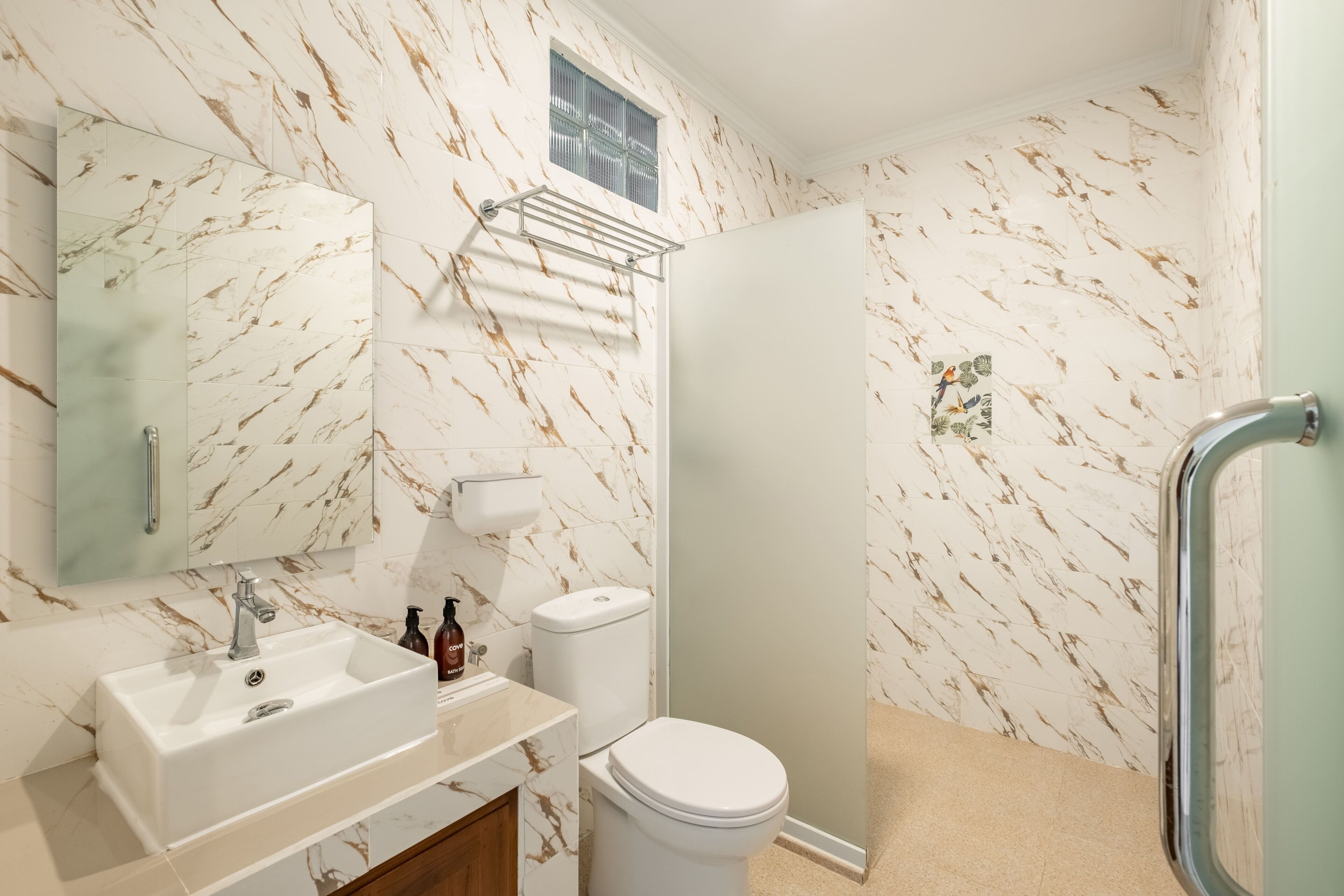A bathroom with a marble-patterned wall, a white sink, a toilet, and a glass-enclosed shower.
