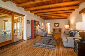 Amplia sala de estar con piso de madera, techo alto con vigas a la vista, chimenea y zona de estar con sofá y sillones.